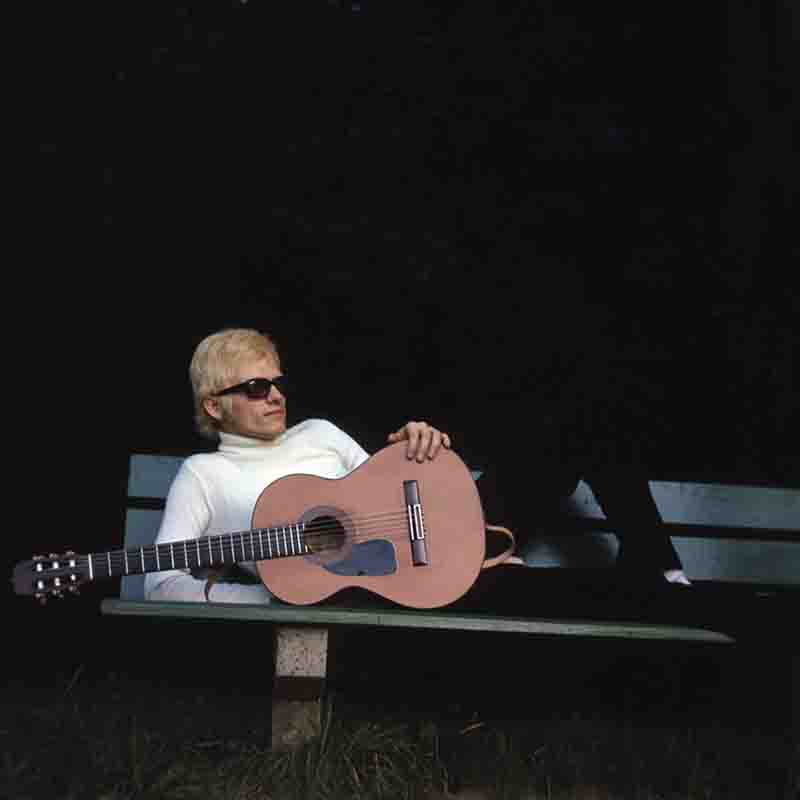 Ein Porträt des deutschen Schlagersängers Heino, fotografiert von Ingeborg Bock-Schroeder. Er liegt mit seiner Gitarre auf einer Parkbank.